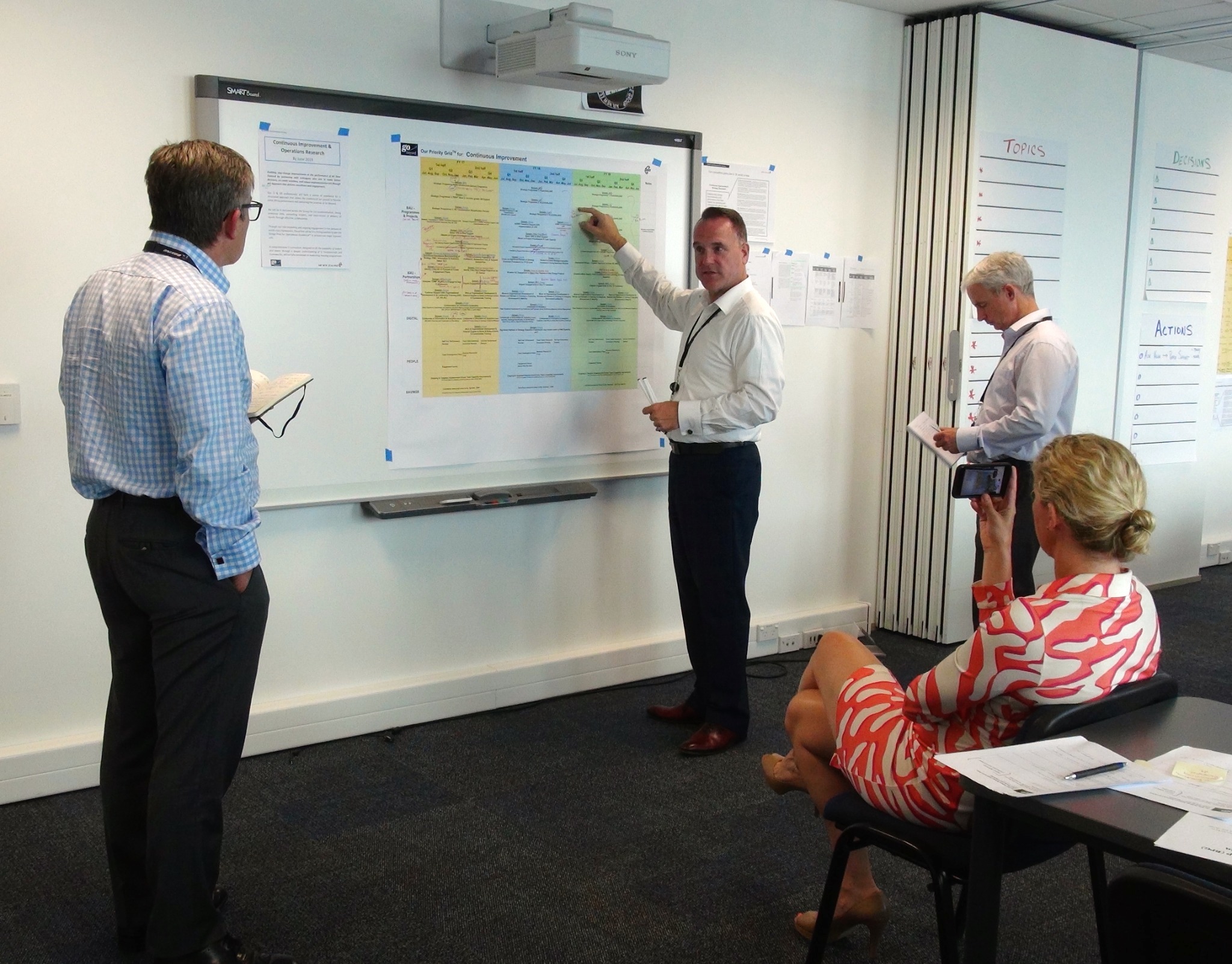 Senior leaders examining a Continuous Improvement board together during a focused working session