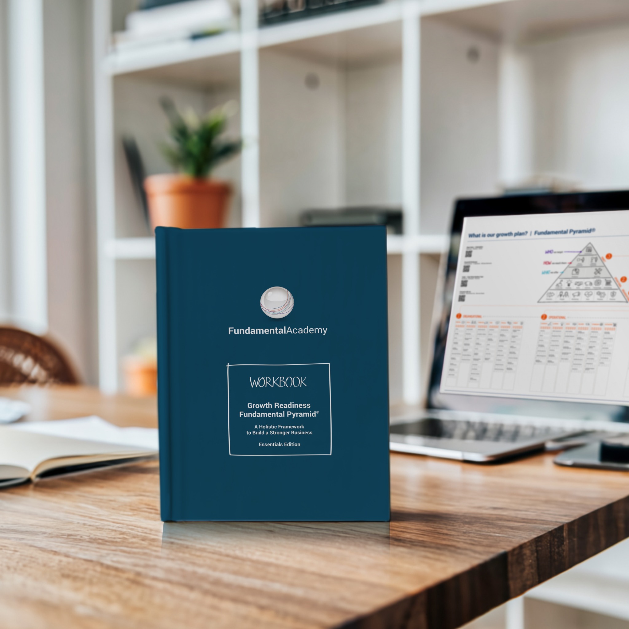 Fundamental Pyramid seminar workbook standing on an office desk beside a laptop.